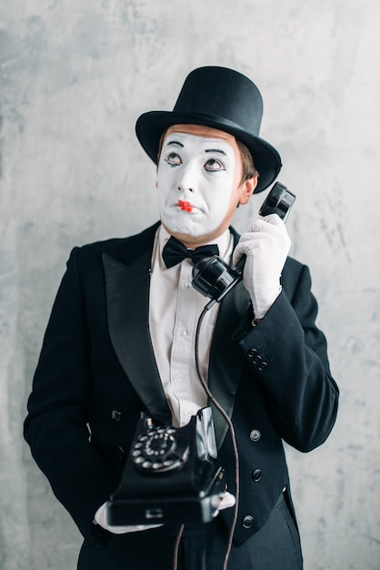 Pantomime-theateracteur met make-upmasker die met retro telefoon presteert.