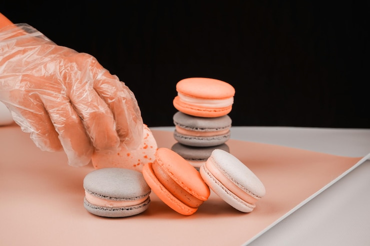 Photo pantone palette a confectioners hand in a transparent glove arranges macarons in a row for a photo on the table on pink paper the confectioner arranges the prepared french dessert