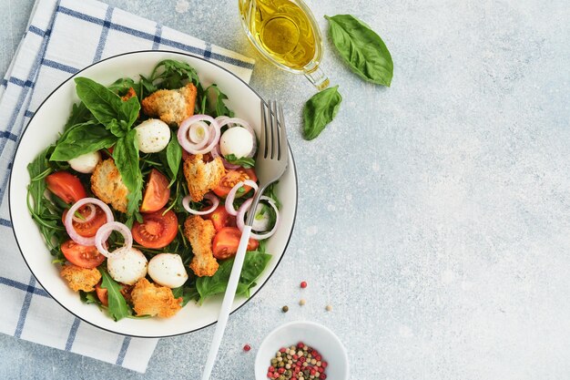 Panzanella italian bread salad traditional food of italy with\
tomatoes mozzarella balls basil onion and bread on light grey\
background traditional italian cooking top view copy space