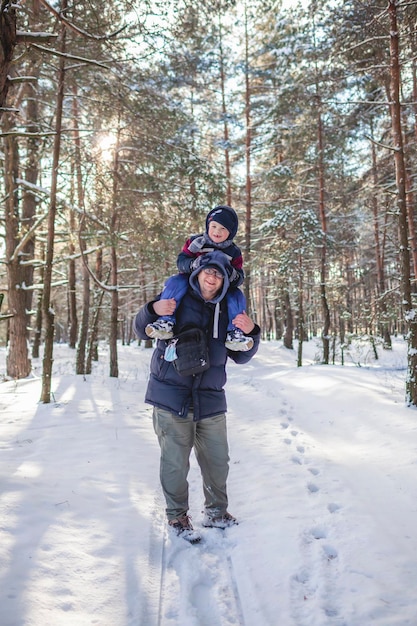 Papa draagt zijn zoontje op zijn schouders zodat hij bij de tak kan en sneeuw van de boom kan schudden