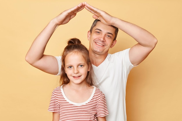 Papa en schooldochter gelukkig samen familie veiligheidszorg concept maken handen dak boven klein meisje hoofd geïsoleerd op beige achtergrond