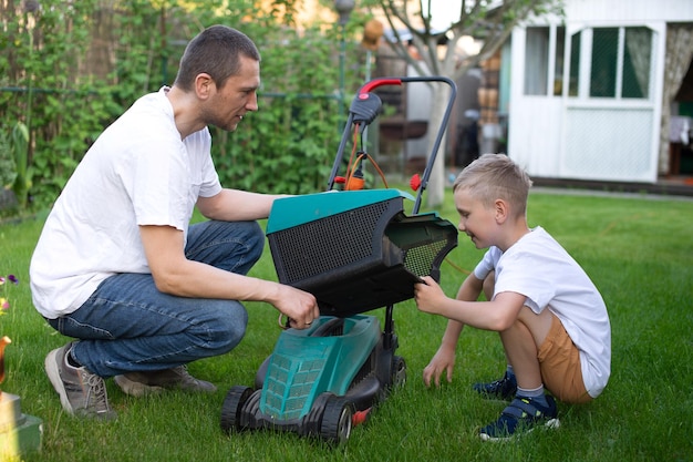 Papa en zijn nieuwsgierige zoon maaien het gazon Demonteer de grasmaaier