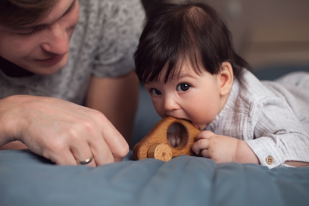 Papa en zijn zoontje liggen op bed en spelen met een houten speelgoedauto