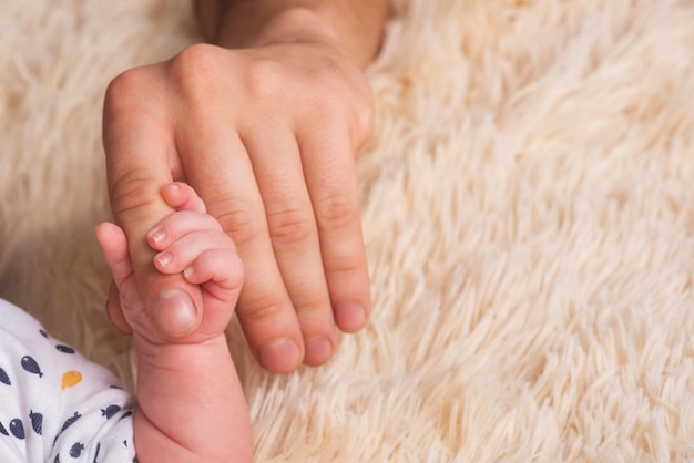 Papa houdt een kleine babyhand in zijn handen. Kleine hand van een pasgeboren baby in grote handen van papa. Baby houdt vaders vinger vast