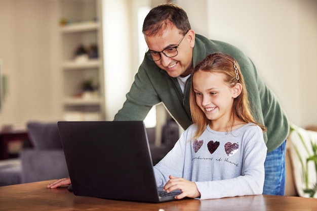 Papa, kom en zie deze foto van een schattig klein meisje dat thuis een laptop gebruikt terwijl haar vader haar helpt