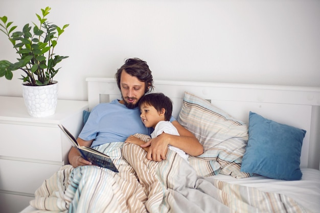 Papa leest een boek voor dat in een wit bed ligt aan zijn zoon voordat hij naar bed gaat