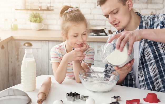 Papa met dochter bakt samen cake in de keuken, giet meel in kom volgens recept, kopieer ruimte