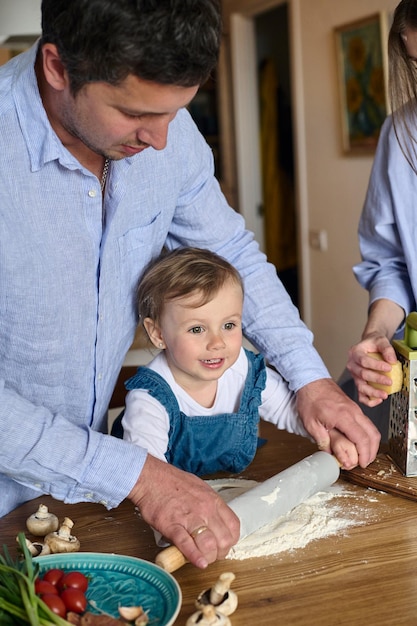 Papa, moeder en hun dochter koken samen pizza in de keuken Het concept van een gelukkig gezin