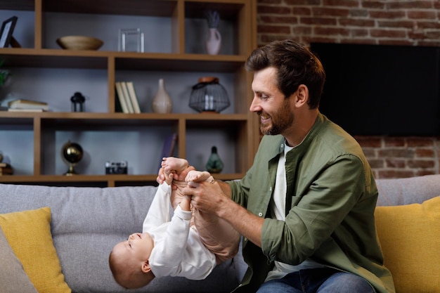 Papa speelt met zijn kleine baby op de bank in een gezellig appartement Vaderlijke liefde Vader knuffelt en kust zijn dochtertje