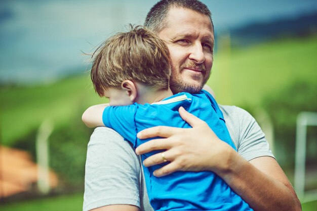 Papa zal er altijd zijn om je op te halen shot van een vrolijke man van middelbare leeftijd die zijn kleine jongen in zijn armen buiten houdt tijdens een bewolkte dag