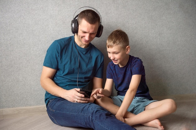 Papa zit met koptelefoon op de grond met de telefoon naast zijn zoon