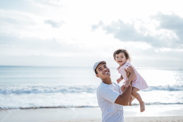 Papa zwaait zijn peutermeisje de lucht in op het strand en heeft samen plezier