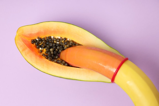 Papaya and banana with condom on violet background