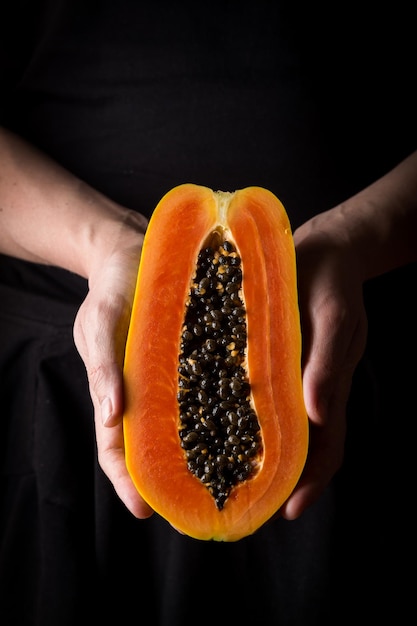 Papaya exotic fruit from Asia. One half of tropical fruit in a man's hand on dark background.