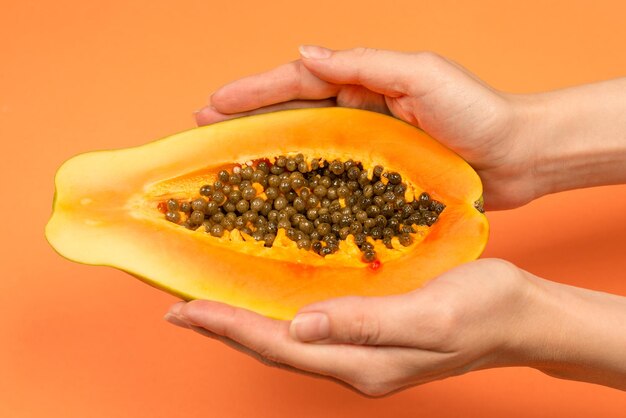 Papaya fruit on a orange background in woman hands. Tropical fruit. Half papaya.