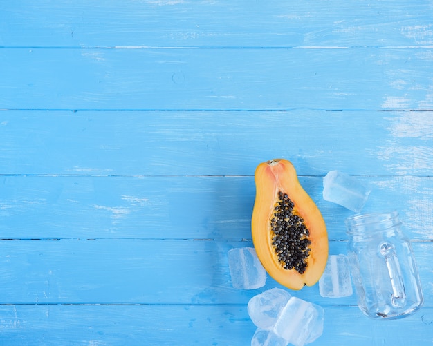 Papaya in tweeën gesneden, glazen pot en ijs, samenstelling van bovenaf, blauwe ruimte concept van versheid