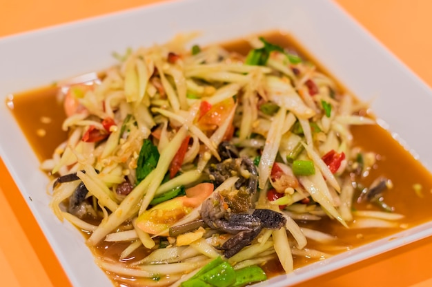 Papaya salad or som-tam in a plate is placed on the orange table.