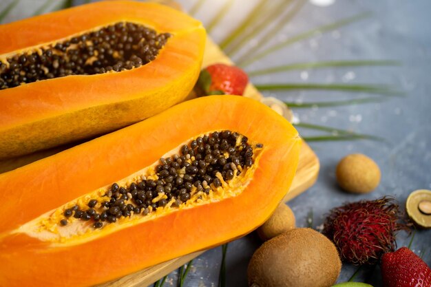 Papaya. Tropical Fruits. Close up shot of two halves of ripe papaya with seeds on wooden cutting board. Sliced papaya and other exotic fruits on table. Top view.