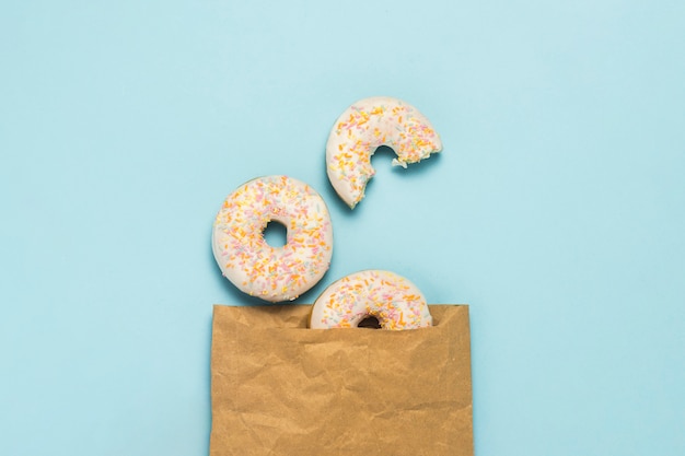 Paper bag and Fresh tasty sweet donuts on a blue background. Concept of fast food, bakery, breakfast, sweets. Minimalism. Flat lay, top view.