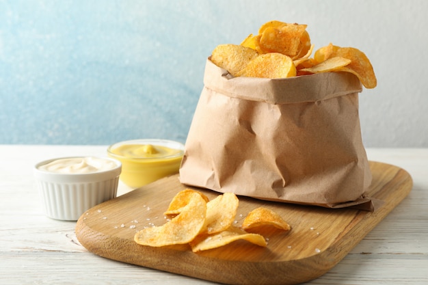 Paper bag of potato chips. Beer snacks, sauce on cutting board, on white wooden, space for text