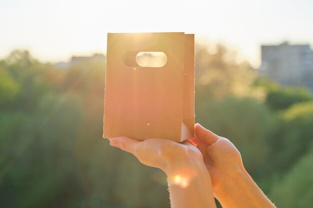 Photo paper bag for shopping in womans hand, background sunset