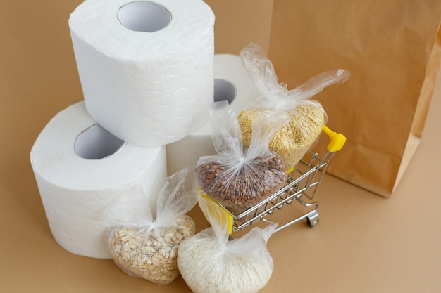 Paper bag toilet paper and various groats in bags in a grocery cart on a brown background