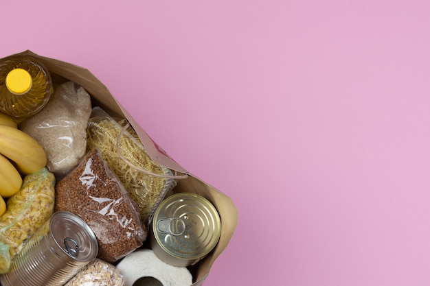 Paper bag with a crisis food supply for the period of quarantine isolation on a pink background