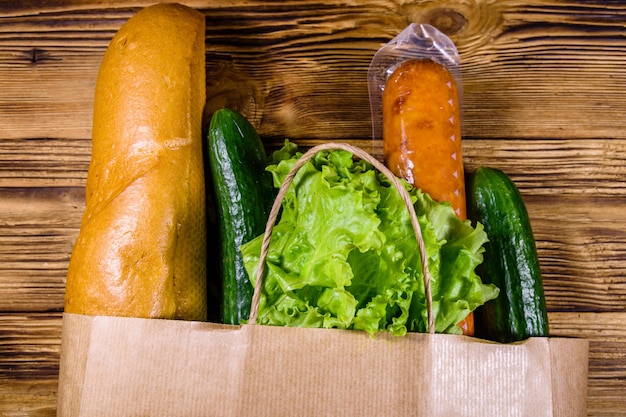 Paper bag with different food from grocery on a wooden table. Supermarket shopping concept. Top view