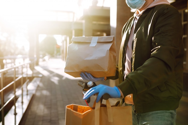 The paper bag with food and coffee in the hands of the courier in quarantine city. Delivery service under quarantine, disease outbreak, coronavirus covid-19 pandemic conditions.