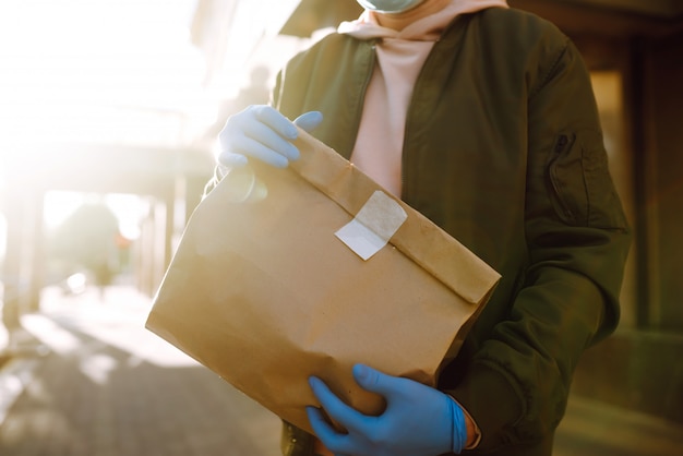 Photo the paper bag with food and coffee in the hands of the courier in quarantine city. delivery service under quarantine, disease outbreak, coronavirus covid-19 pandemic conditions.