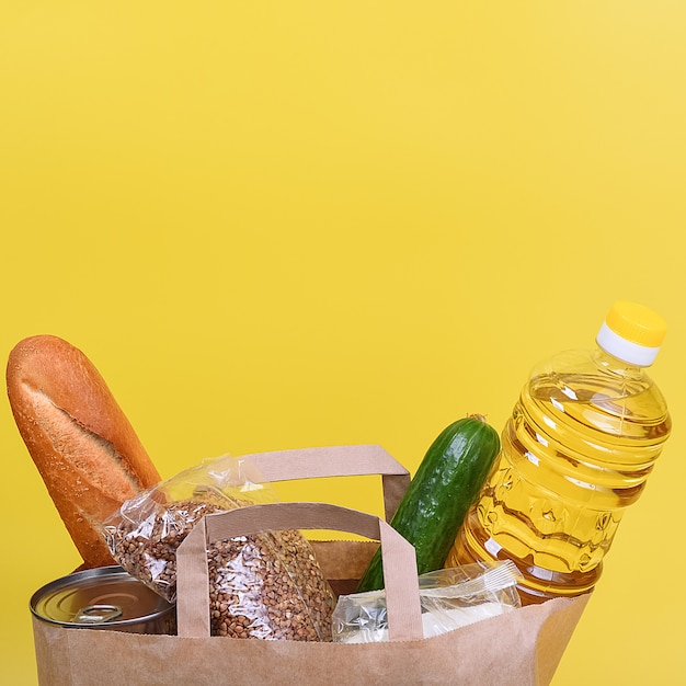 Paper bag with food supplies for the period of quarantine isolation on a yellow background. Copyspace.