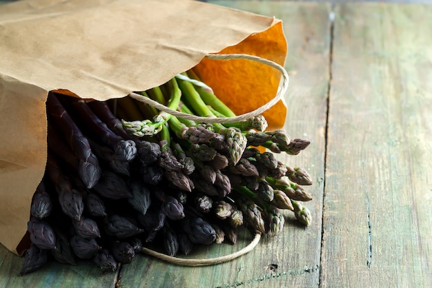 Paper bag with freshly picked raw organic natural purple asparagus spears on a wooden background.