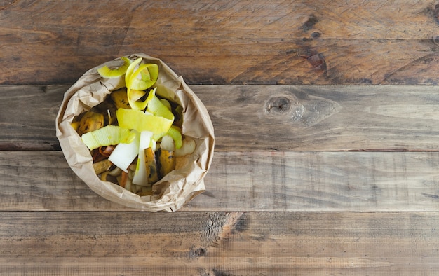 Sacchetto di carta con bucce di frutta su fondo in legno per compostaggio.