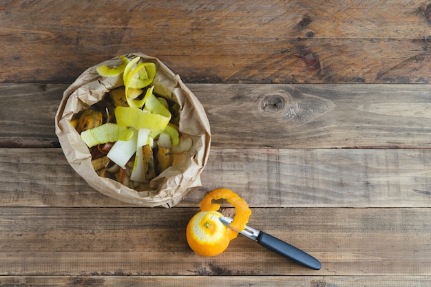 Sacchetto di carta con bucce di frutta su fondo in legno per compostaggio.