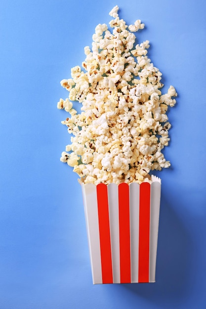 Paper bag with popcorn on color background