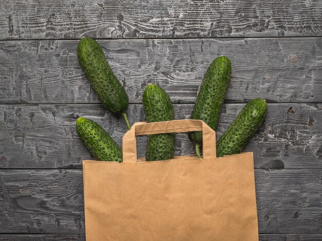 Photo a paper bag with spilled cucumbers on a wooden table. fresh vegetables in eco-friendly packaging.