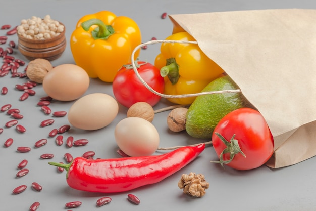 Paper bag with walnuts, chickpeas, beans, lentils, peppers, tomatoes, avocado on a gray background