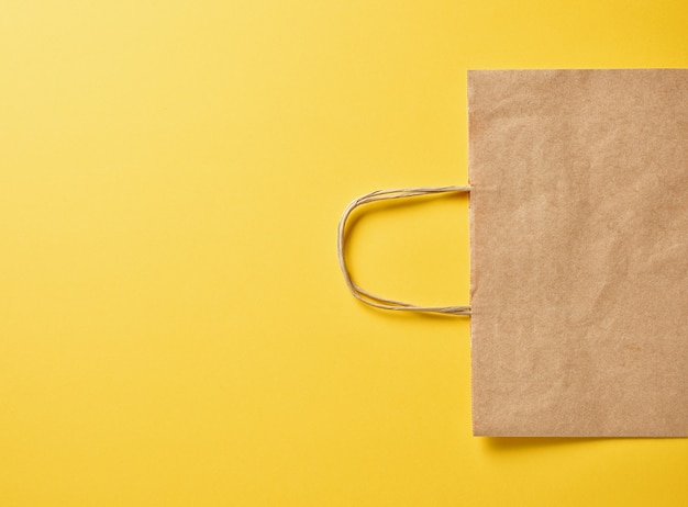 Paper bag on yellow background, top view