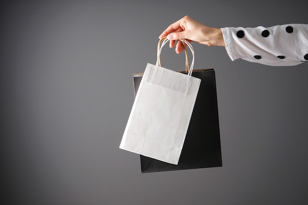 Paper black and white craft bag, eco packaging in a female hand\
on a gray background, place for text.