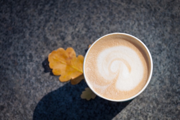 Paper blue coffee cup on the autumn fall leaves and stone grey 