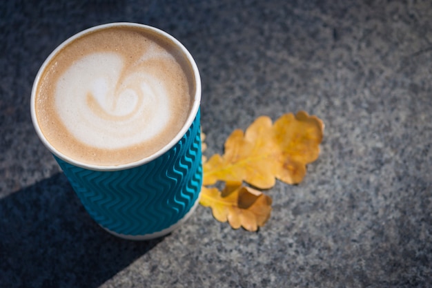 Paper blue coffee cup on the autumn fall leaves and stone grey 