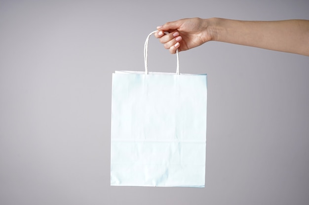 Paper blue craft bag, eco packaging in a female hand on a gray
background. place for text.