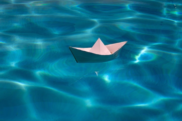 Paper boat sailing on blue water surface paper ship sail paper boat on the sea water background drea