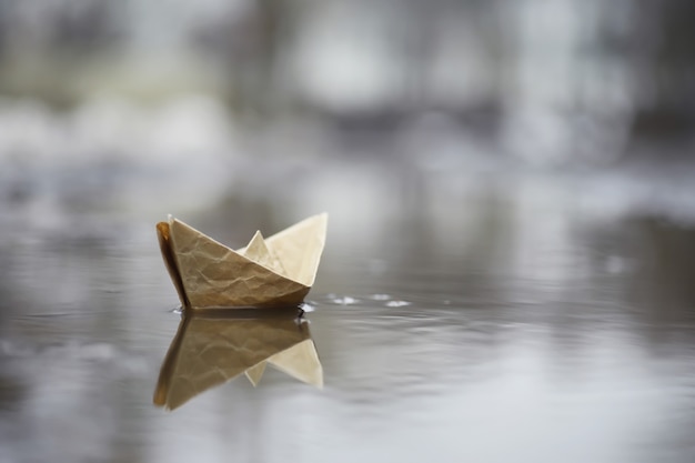 Photo paper boat in the water on the street. the concept of early spring. melting snow and an origami boat on water waves.