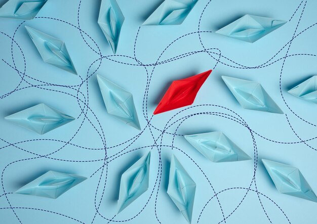 Paper boats on a blue background with paths of movement representing the concept of individuality