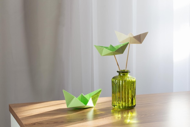 paper boats in green glass vase on wooden table