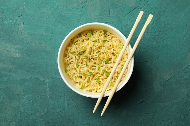 Paper bowl with noodles and chopsticks on green textured background