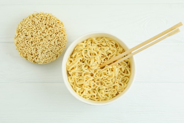 Paper bowl with noodles and chopsticks on white wooden background