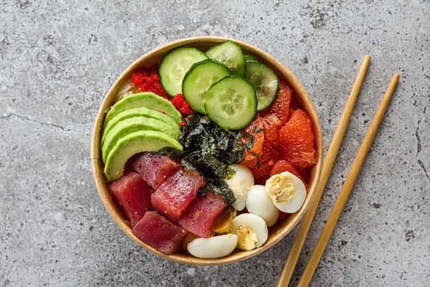 Paper box or package with tuna poke bowl salad with avocado for take away or food delivery with chopsticks on gray background top view Healthy food