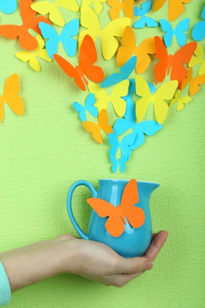 Photo paper butterflies fly out of pitcher on green wall background